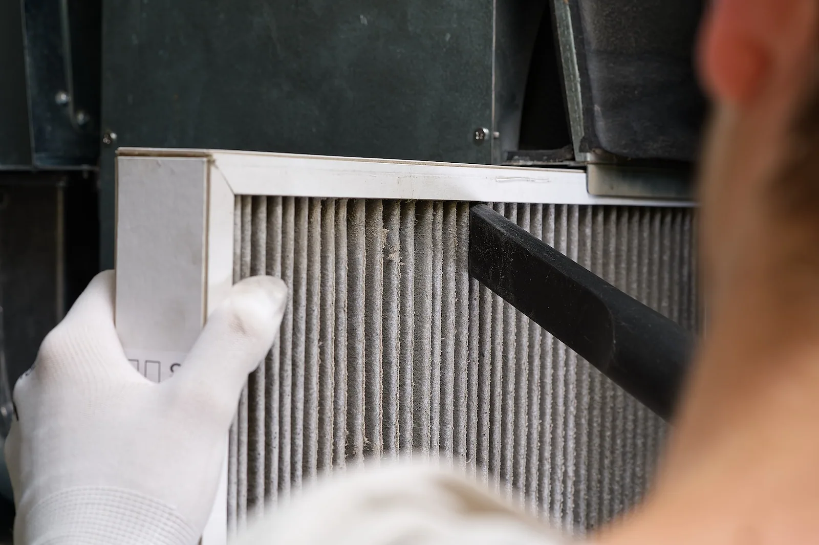 Vacuuming dust from a pleated furnace filter during a maintenance visit