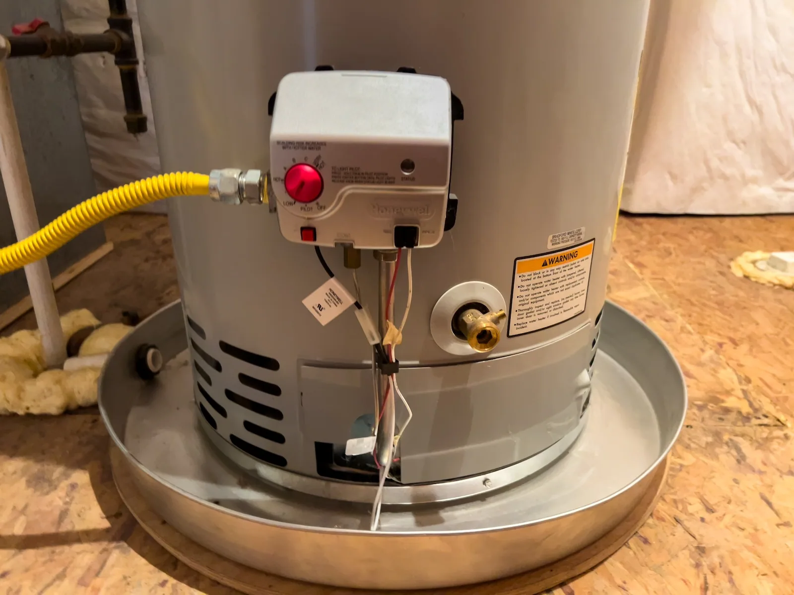Newly installed Bradford White gas water heater sitting in a drip pan with its flexible gas line connected